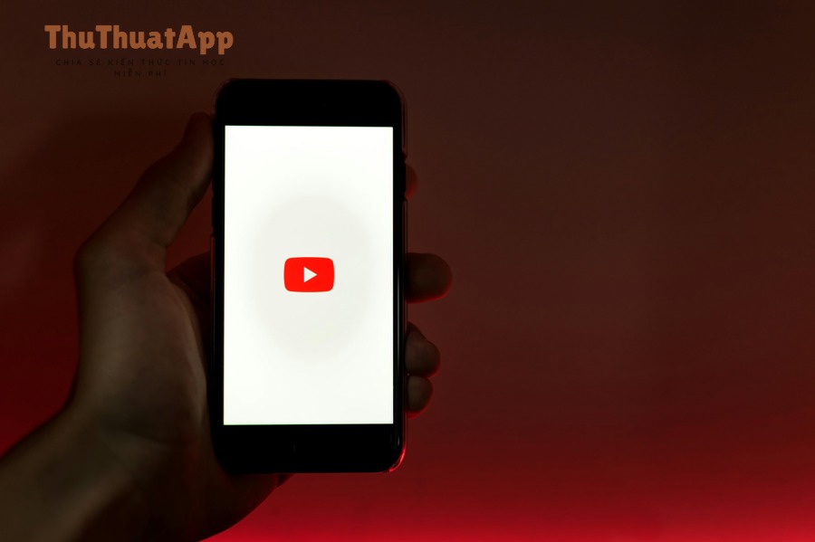 Người dùng cầm điện thoại với biểu tượng YouTube, minh họa hành vi tìm kiếm và nhấp